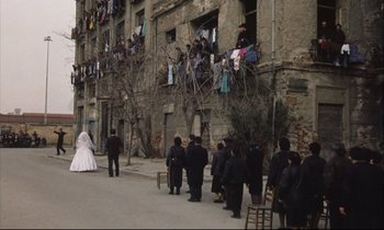 Movie still from “Eternity and a Day” (1998), directed by Theodoros Angelopoulos – A group of people standing on the side of a building; Extreme Wide shot, High angle