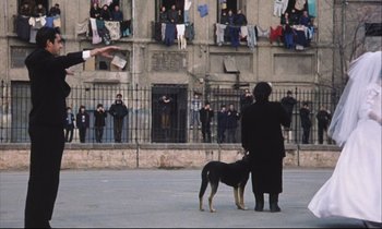 Movie still from “Eternity and a Day” (1998), directed by Theodoros Angelopoulos – Two people and a dog in front of a building; Wide shot, Low angle