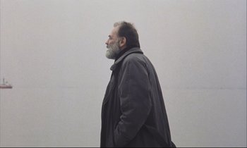 Movie still from “Eternity and a Day” (1998), directed by Theodoros Angelopoulos – A man with a gray beard is standing in a white room; Medium shot, Low angle