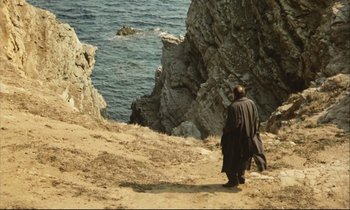 Movie still from “Eternity and a Day” (1998), directed by Theodoros Angelopoulos – A man standing on top of a hill next to a body of water; Extreme Wide shot, High angle