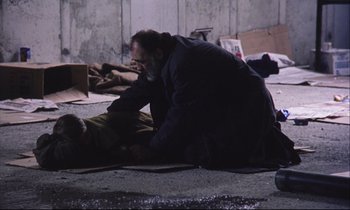Movie still from “Eternity and a Day” (1998), directed by Theodoros Angelopoulos – A man kneeling down on the ground next to another man; Wide shot, High angle