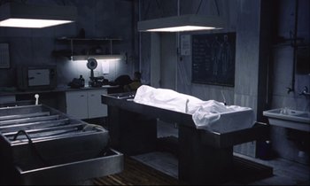 Movie still from “Eternity and a Day” (1998), directed by Theodoros Angelopoulos – A autopsy table in an autopsy room with a man working in the background; Wide shot, High angle