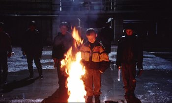 Movie still from “Eternity and a Day” (1998), directed by Theodoros Angelopoulos – A group of people standing around a fire at night; Wide shot, Low angle