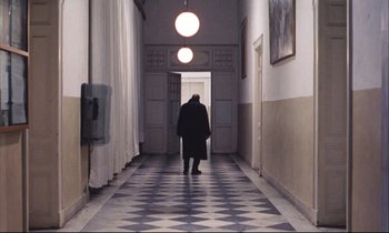 Movie still from “Eternity and a Day” (1998), directed by Theodoros Angelopoulos – A person walking down a hall way in a building; Wide shot, High angle