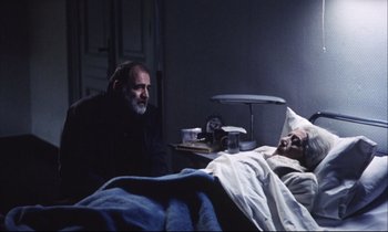 Movie still from “Eternity and a Day” (1998), directed by Theodoros Angelopoulos – An older man sitting next to an older woman in a bed; Medium shot, High angle