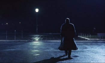 Movie still from “Eternity and a Day” (1998), directed by Theodoros Angelopoulos – A man in a long coat walking in the dark at night; Wide shot, Low angle