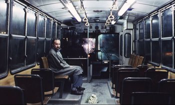 Movie still from “Eternity and a Day” (1998), directed by Theodoros Angelopoulos – A man sitting on a bus with a bouquet of flowers in his lap; Wide shot, High angle