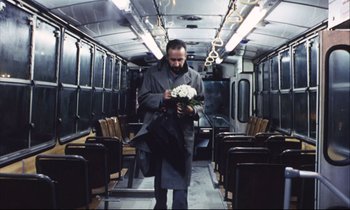 Movie still from “Eternity and a Day” (1998), directed by Theodoros Angelopoulos – A man walking down a train holding a bouquet of flowers; Wide shot, High angle
