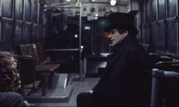 Movie still from “Eternity and a Day” (1998), directed by Theodoros Angelopoulos – A man sitting on a bus wearing a black hat; Medium shot, High angle