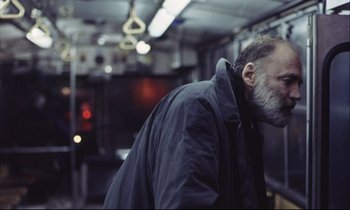 Movie still from “Eternity and a Day” (1998), directed by Theodoros Angelopoulos – A man with a gray beard is standing on a train; Close Up shot, Over the shoulder angle