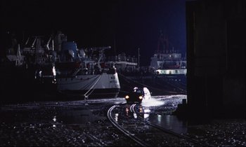 Movie still from “Eternity and a Day” (1998), directed by Theodoros Angelopoulos – A car driving down a street next to a dock; Extreme Wide shot, High angle