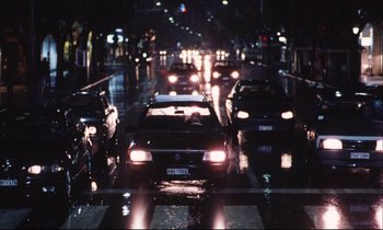 Movie still from “Eternity and a Day” (1998), directed by Theodoros Angelopoulos – Cars driving down a street at night in the rain; Wide shot, High angle