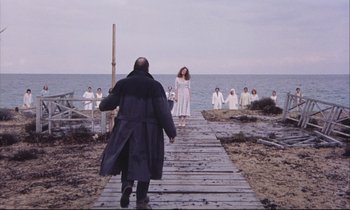 Movie still from “Eternity and a Day” (1998), directed by Theodoros Angelopoulos – A group of people standing on a dock near the ocean; Wide shot, Low angle
