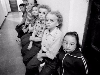 Movie still from “Even Dwarfs Started Small” (1970), directed by Werner Herzog – A black and white photo of a group of people sitting in a row; Wide shot, High angle