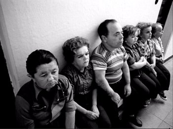 Movie still from “Even Dwarfs Started Small” (1970), directed by Werner Herzog – A group of people sitting in a row on a wall; Wide shot, High angle
