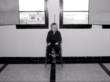 Movie still from “Even Dwarfs Started Small” (1970), directed by Werner Herzog – A little boy sitting in a chair in front of a window; Wide shot, High angle