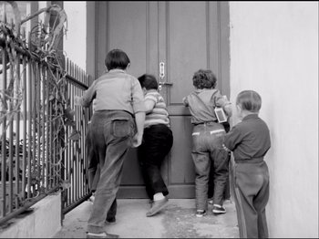 Movie still from “Even Dwarfs Started Small” (1970), directed by Werner Herzog – A group of kids standing in front of a wooden door; Medium shot, High angle