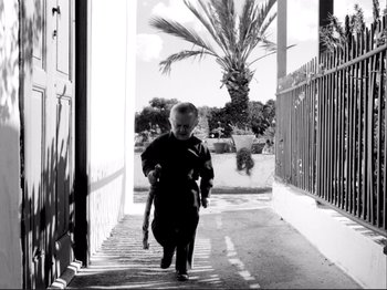 Movie still from “Even Dwarfs Started Small” (1970), directed by Werner Herzog – A little boy walking down a sidewalk holding a cane; Wide shot, Low angle