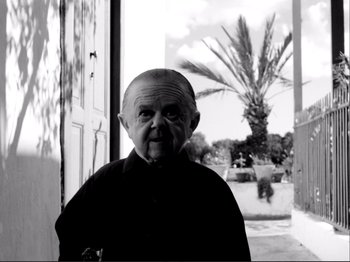 Movie still from “Even Dwarfs Started Small” (1970), directed by Werner Herzog – An older man standing in front of a palm tree; Medium shot, Low angle