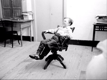 Movie still from “Even Dwarfs Started Small” (1970), directed by Werner Herzog – A young boy sitting in a chair listening to music; Wide shot, High angle