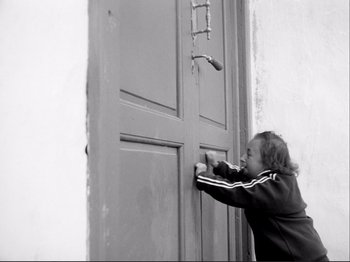 Movie still from “Even Dwarfs Started Small” (1970), directed by Werner Herzog – A young child is knocking on a door; Medium shot, Low angle