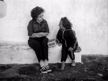 Movie still from “Even Dwarfs Started Small” (1970), directed by Werner Herzog – A woman sitting next to a little girl on a ledge; Medium shot, High angle