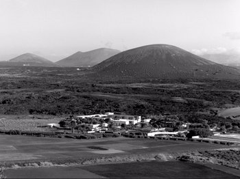 Movie still from “Even Dwarfs Started Small” (1970), directed by Werner Herzog – A black and white photo of a town with a mountain in the background; Extreme Wide shot, High angle