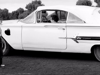 Movie still from “Even Dwarfs Started Small” (1970), directed by Werner Herzog – An old car with a woman sitting in the driver's seat; Wide shot, High angle