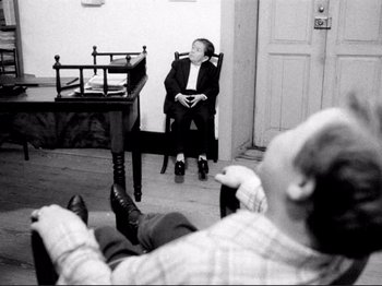 Movie still from “Even Dwarfs Started Small” (1970), directed by Werner Herzog – A man sitting on a chair in a room; Wide shot, High angle