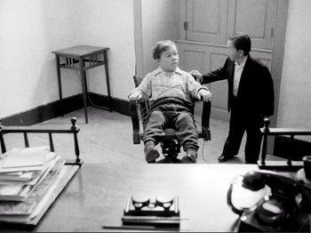 Movie still from “Even Dwarfs Started Small” (1970), directed by Werner Herzog – A boy sitting in a chair next to another boy; Medium shot, High angle