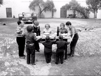 Movie still from “Even Dwarfs Started Small” (1970), directed by Werner Herzog – A group of people standing around a table with food on it; Wide shot, High angle