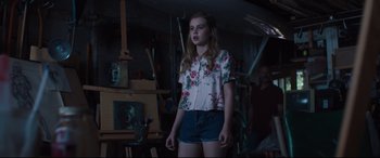 Movie still from “Every Day” (2018), directed by Michael Sucsy – A woman standing in front of a painting in a room; Medium shot, Over the shoulder angle