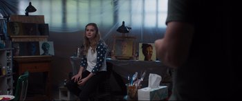 Movie still from “Every Day” (2018), directed by Michael Sucsy – A woman sitting in front of a table with a painting on it; Medium shot, Over the shoulder angle
