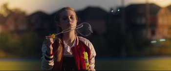 Movie still from “Every Day” (2018), directed by Michael Sucsy – A young girl blowing a bubble with a bubble wand; Medium shot, Over the shoulder angle