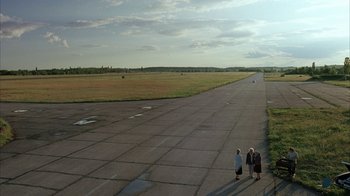 Movie still from “Everything Is Illuminated” (2005), directed by Liev Schreiber – Three people are standing on the tarmac of an airport; Extreme Wide shot, High angle
