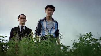 Movie still from “Everything Is Illuminated” (2005), directed by Liev Schreiber – A man standing next to another man in a field of plants; Medium shot, Low angle