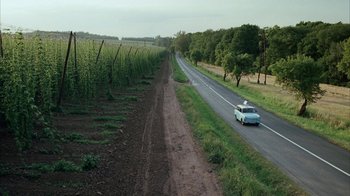 A car driving down a road near a field of grass