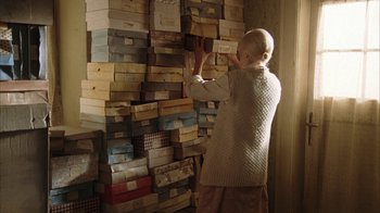 Movie still from “Everything Is Illuminated” (2005), directed by Liev Schreiber – An older woman is reaching up to pick up a shoe box; Wide shot, High angle
