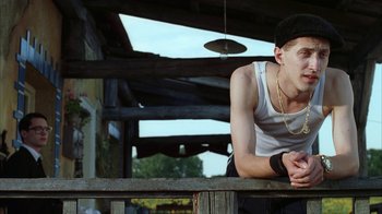 Movie still from “Everything Is Illuminated” (2005), directed by Liev Schreiber – A man leaning on a wooden rail in front of a building; Medium shot, Low angle
