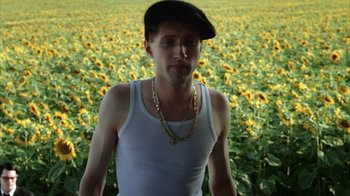 Movie still from “Everything Is Illuminated” (2005), directed by Liev Schreiber – A man in a white tank top standing in front of a field of sunflowers; Medium shot, Low angle