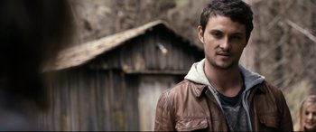 Movie still from “Evil Dead” (2013), directed by Fede Alvarez – A man in a brown jacket standing in front of a wooden building; Close Up shot, Over the shoulder angle