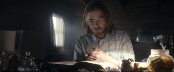 Movie still from “Evil Dead” (2013), directed by Fede Alvarez – A man sitting in front of an open book; Medium shot, Low angle