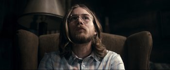 Movie still from “Evil Dead” (2013), directed by Fede Alvarez – A man with long hair and glasses sitting on a couch; Close Up shot, Over the shoulder angle