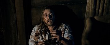 Movie still from “Evil Dead” (2013), directed by Fede Alvarez – A man with long brown hair and a beard is holding a drink; Medium shot, Overhead angle