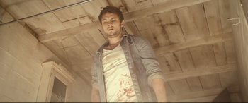Movie still from “Evil Dead” (2013), directed by Fede Alvarez – A man in a white t - shirt is standing in a room; Medium shot, Low angle