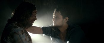 Movie still from “Evil Dead” (2013), directed by Fede Alvarez – A man with a bloody face is being held by another man in a dark room; Close Up shot, Over the shoulder angle
