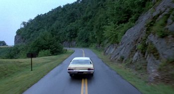 Movie still from “Evil Dead II” (1987), directed by Sam Raimi – A car driving down a road near some trees; Extreme Wide shot, High angle