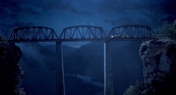 Movie still from “Evil Dead II” (1987), directed by Sam Raimi – A train crossing a bridge over a body of water at night; Extreme Wide shot, Overhead angle