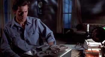 Movie still from “Evil Dead II” (1987), directed by Sam Raimi – A man sitting in front of a projector in front of a window; Medium shot, Low angle