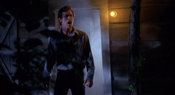 Movie still from “Evil Dead II” (1987), directed by Sam Raimi – A man standing in front of a door with his mouth open; Medium shot, Low angle
